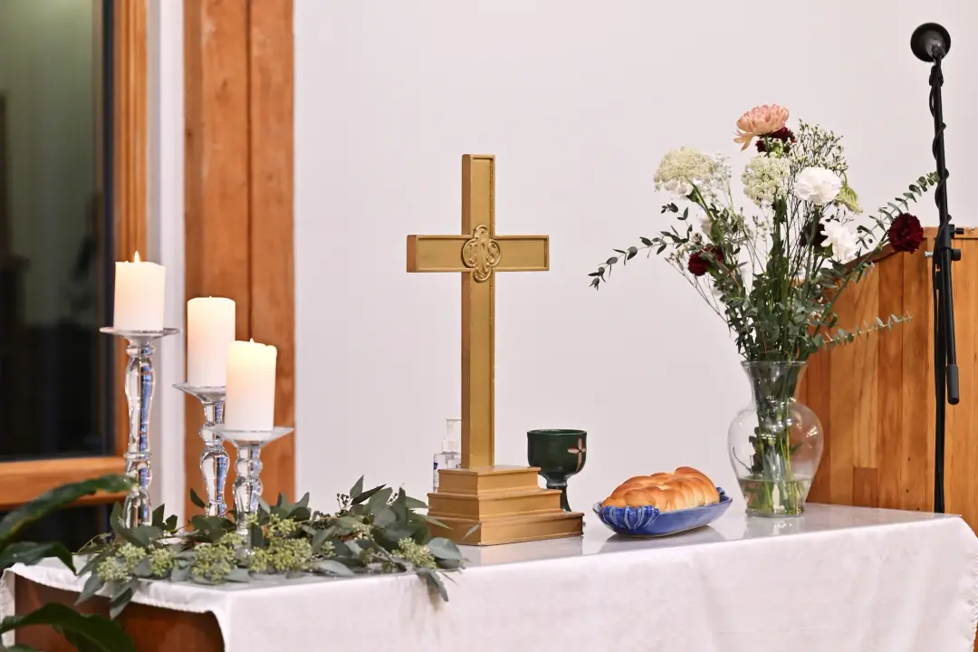 Wooden lectern decorated with greenery, with the cross and windows behind it